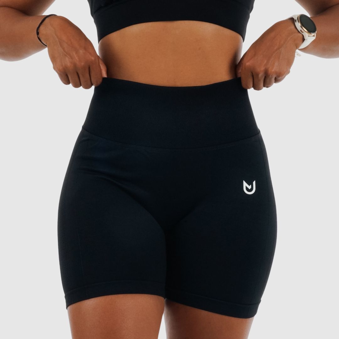 Frau trägt schwarze nahtlose High-Waist-Shorts mit weißem Sneaker – Produktbild frontal.